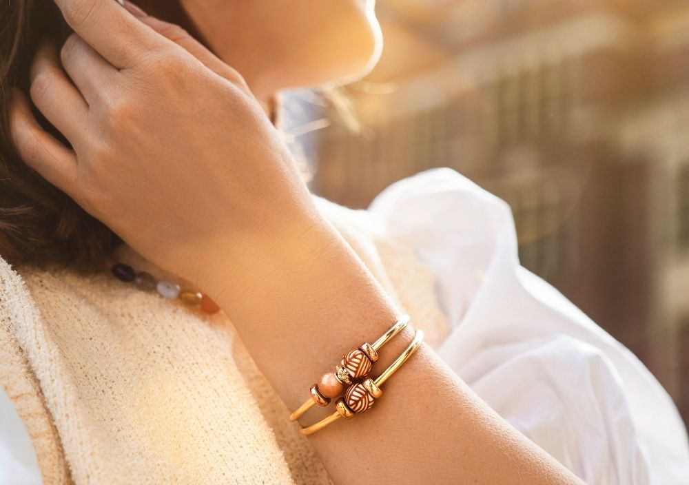 Bližnji posnetek dveh pozlačenih zapestnic, okrašenih z obeski, v poletni sončni svetlobi.