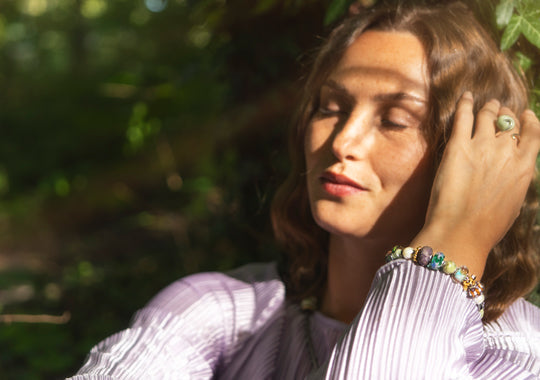 Woman with hand on head, wearing a colorful bracelet, in a natural setting